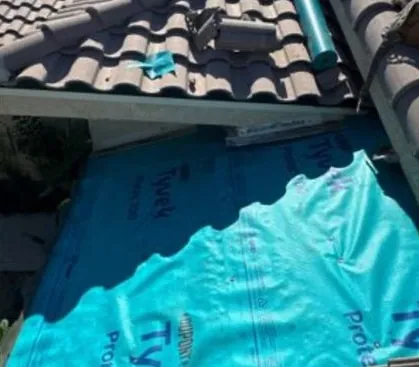 Blue Tyvek underlayment laid over a roof deck below an edge of barrel tile and a dark fascia