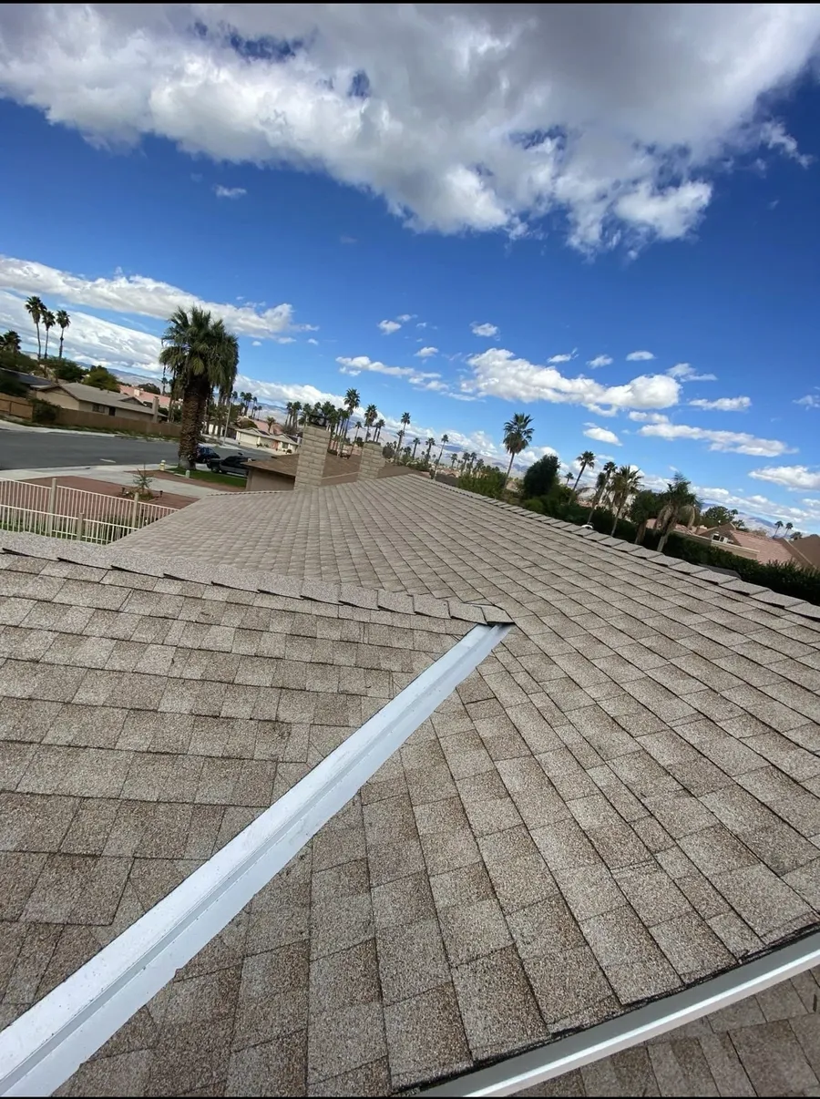 A tan architectural shingle roof meeting its ridge, desert homes and mountains beyond