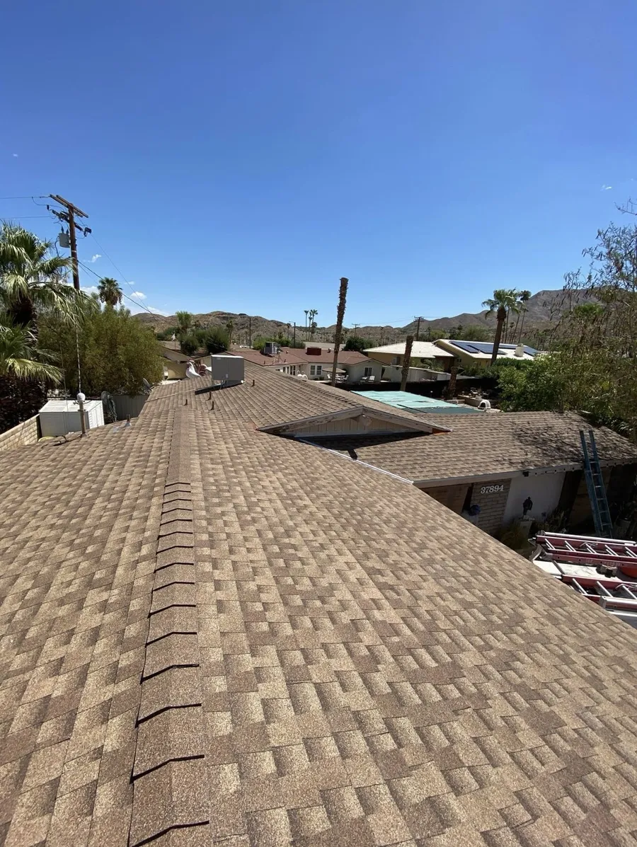 A tan shingle roof and ridge with a ladder resting at the eave, mountains behind
