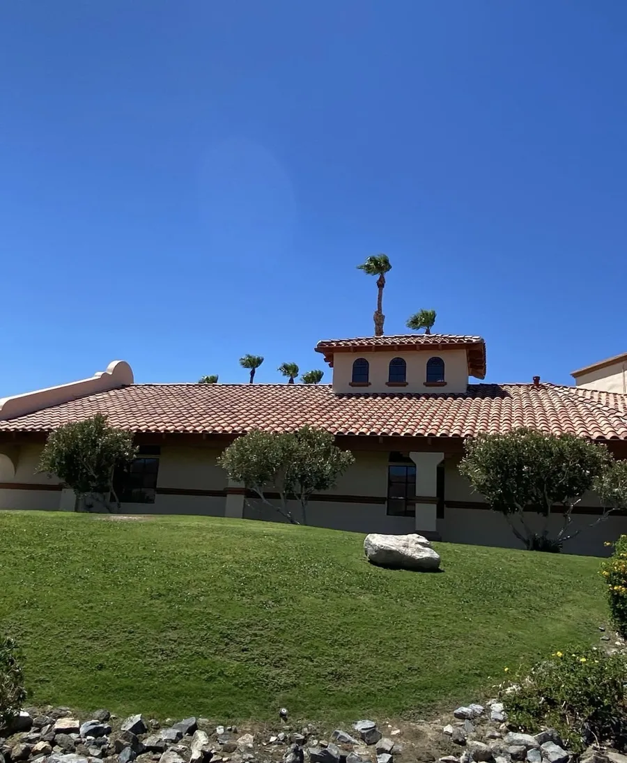 A tile-roofed home seen across its front lawn, desert boulders and palms around it