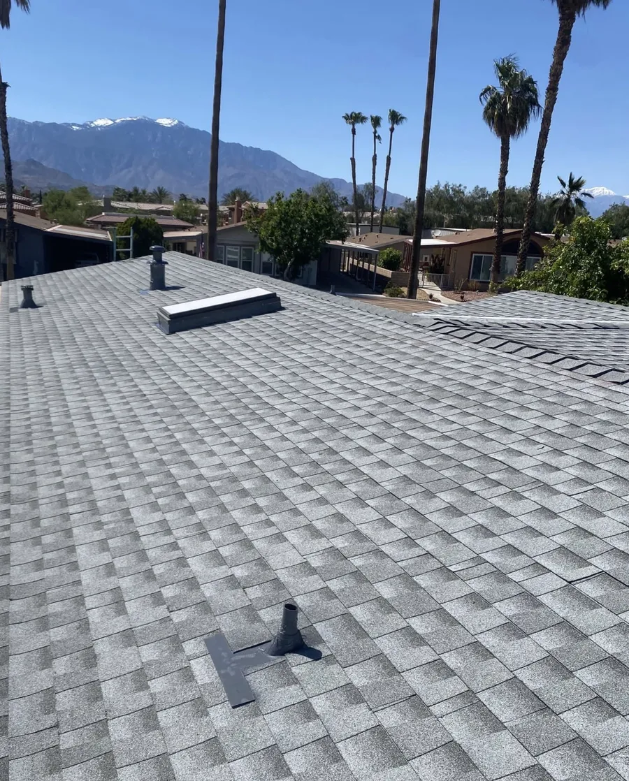 A grey shingle roof under a clear sky, desert homes and mountains beyond