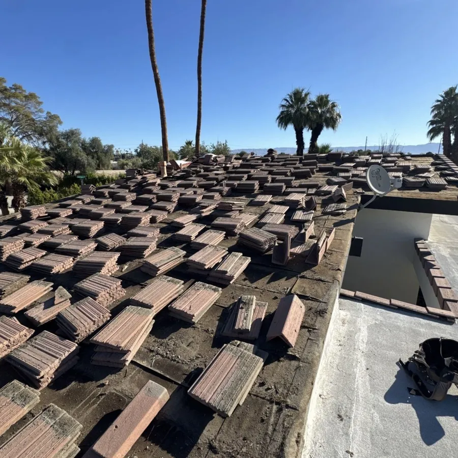 Terracotta tiles lifted and stacked in rows across a low-slope deck during a re-roof