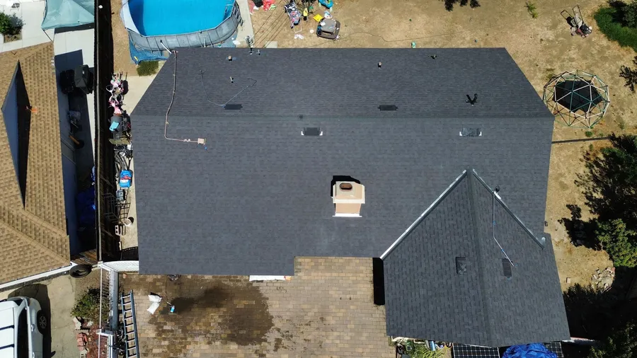 Overhead drone view of a home newly roofed in charcoal architectural shingles, its chimney and roof vents flashed