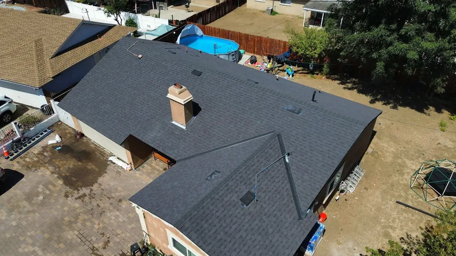 Drone view of a single-storey home with a new charcoal shingle roof, chimney flashed and vents in place, a backyard pool beyond